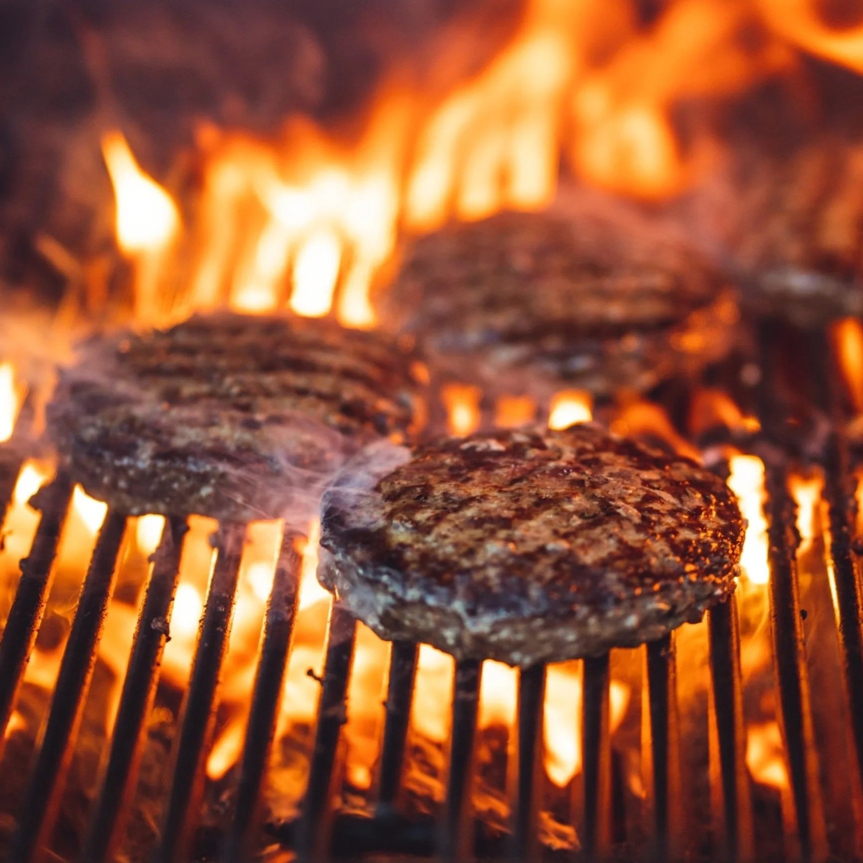 Juicy beef patties grilling over an open flame, creating a smoky aroma and charred texture, perfect for summer barbecues and outdoor cooking.